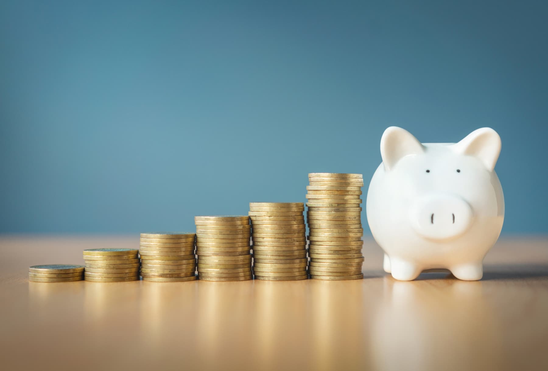 Pilas de monedas ordenadas de menor a mayor, simulando una gráfica de barras que culmina en una alcancía de cochinito, representando el crecimiento financiero y la productividad a través del ahorro