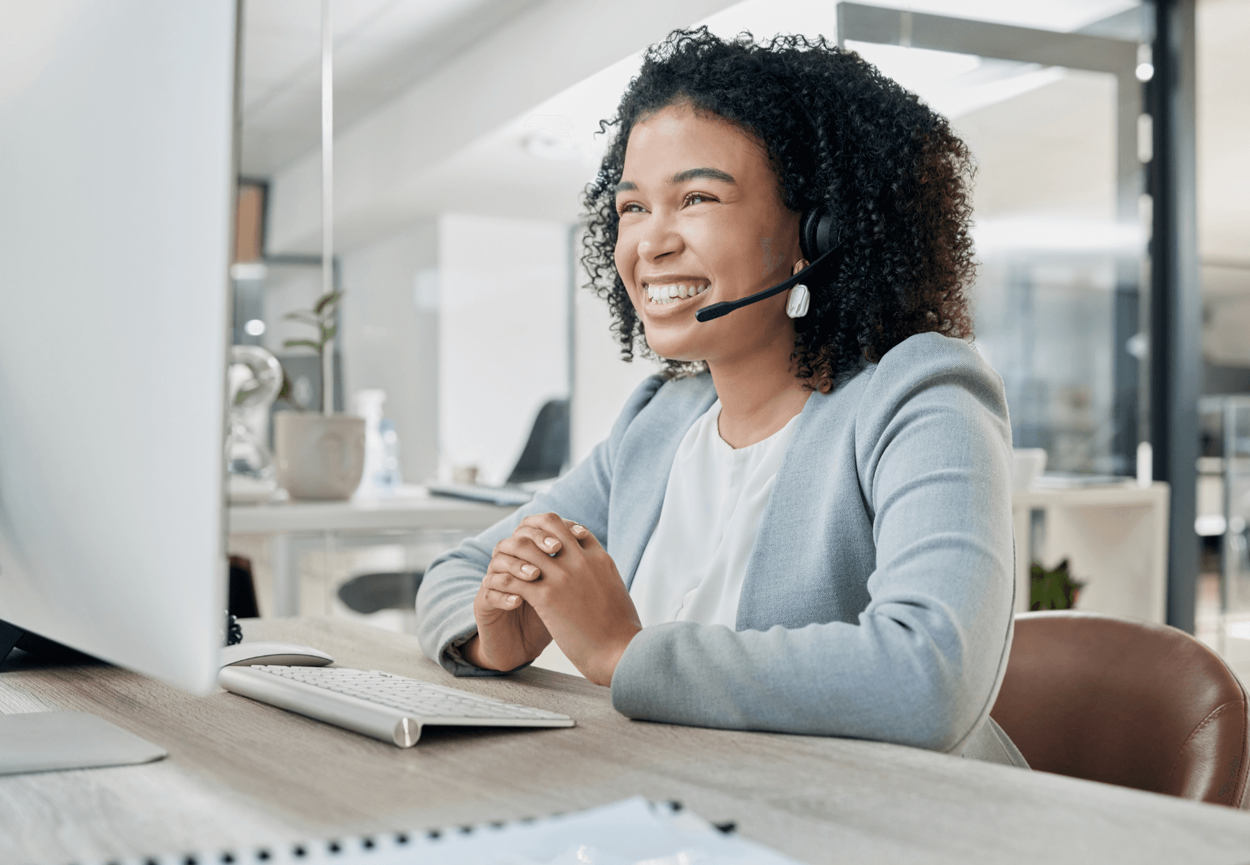 Una mujer con una diadema con audífonos y micrófono está feliz por lo fácil que es la gestión de la comunicación con sus clientes al tener toda la información que necesita a la mano.