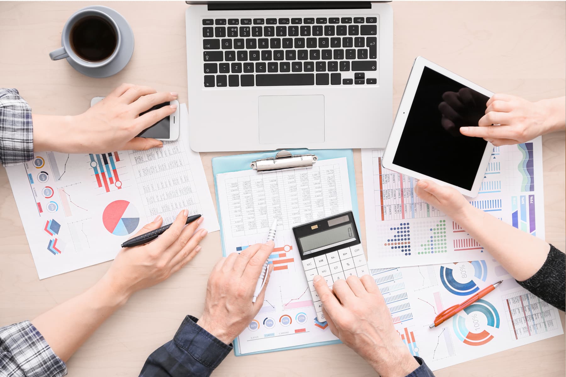 Varias personas analizan gráficas, hacen cálculos en sus calculadoras, con laptops y café a la mano, señalando la información importante de sus gastos para optimizar la automatización y la productividad financiera.